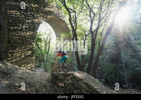 Man riding bike sur sentier par des mur de pierre en forêt Banque D'Images