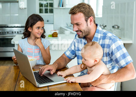 Heureux père à l'aide d'ordinateur portable tout en prenant soin des enfants Banque D'Images