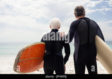 Senior couple in wetsuit holding surfboard on beach Banque D'Images