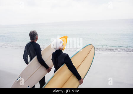 Senior couple in wetsuit holding surfboard on beach Banque D'Images