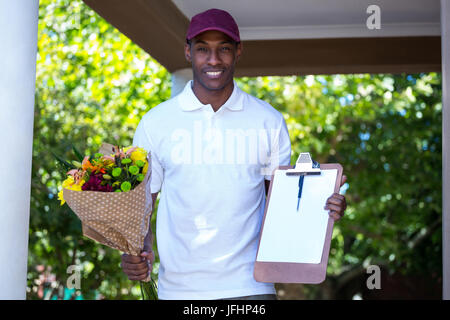 Delivery man holding flower bouquet et presse-papiers Banque D'Images