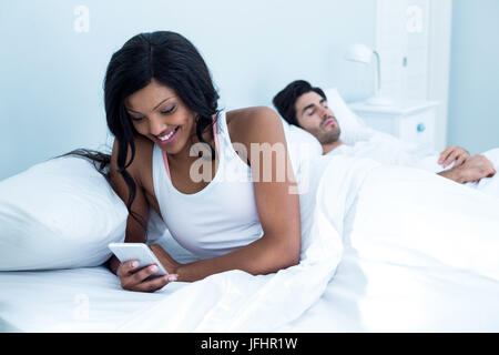 Contrôle de femme son téléphone portable tout en man sleeping on bed Banque D'Images