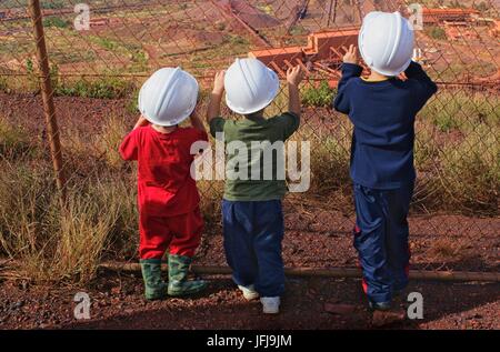 Trois enfants portant des casques de l'exploitation minière à l'intermédiaire d'un grillage à la Mount Tom : La mienne, WA, Australie. Banque D'Images