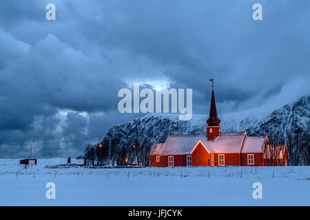 Lumières sur l'église au crépuscule avec les sommets enneigés en arrière-plan Flakstad Lofoten, Norvège Europe Banque D'Images