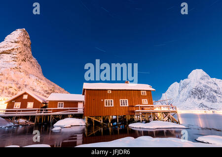 Nuit étoilée sur les pistes enneigées entouré par les maisons de pêcheurs de la mer congelés et Reinevagen Bay Iles Lofoten Norvège Europe Banque D'Images