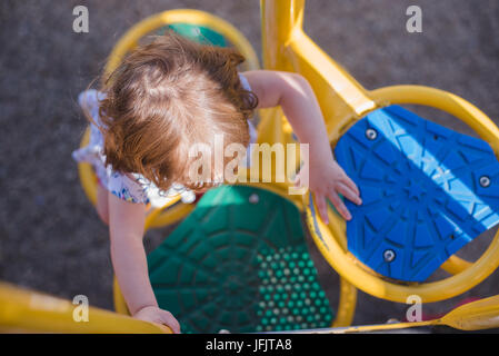 Une jeune fille monte à l'équipement de jeu à la lumière du soleil le port de chaussures rouge vif.