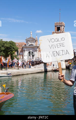 Venise, Vénétie, Italie 02 juillet 2017. Marche de protestation à partir de l'arsenal pour les Vénitiens qui protestent contre la conversion des monuments historiques et des bâtiments de la ville en accomaodation touristiques, restaurants et attractions touristiques, ainsi que la poursuite de la présence de grands paquebots entrant dans la Giudeca canal et port sous le slogan pas Grandi Navi. Un homme tient un écriteau Voglio Vivere a Venezia - je veux vivre dans Venise. Dans l'arrière-plan peut être vu des manifestants de quitter l'Arsenale campo et faire leur chemin au bord de l'eau . Mary crédit Clarke/Alamy Live News Banque D'Images