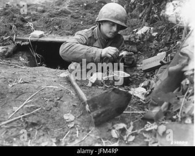 Pvt Mason Armstrong émerge d'un trou du renard quelque part en Allemagne depuis assez longtemps pour se préparer une tasse de ration K café. 1945 Banque D'Images