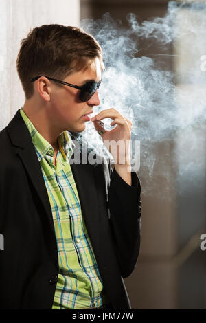 Mode jeune homme à lunettes fumer une cigarette Banque D'Images