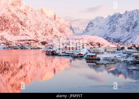 Lever de soleil rose et des sommets enneigés encadrent la mer gelée et le village de pêche Reine Bay Nordland îles Lofoten Norvège Europe Banque D'Images