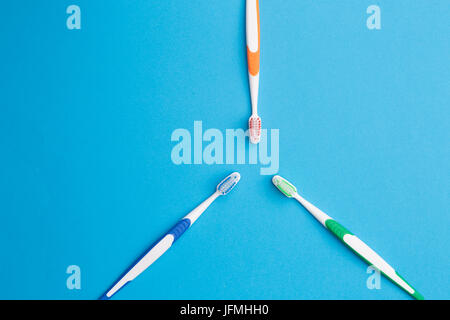 Trois brosses à dents multicolores sur fond bleu vide avec place pour l'écriture. Disposés en forme de triangle Banque D'Images