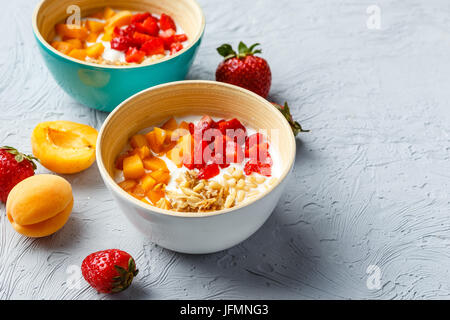 Yogourt nature avec des morceaux d'abricots, fraises, granola et les noix de pin dans deux bols sur fond clair Banque D'Images