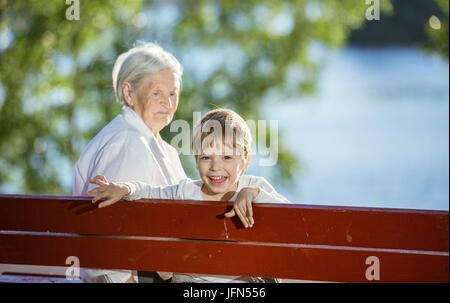 Petit-fils et senior woman having fun while sitting on bench in park Banque D'Images