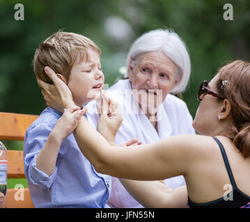 Mère traiter gratter sur le menton de son fils alors qu'il était assis sur un banc dans le parc. hauts grand-mère assise à côté sur le banc. Banque D'Images