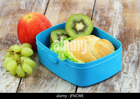 École en santé boîte à lunch sandwich au fromage contenant des fruits : kiwi, pomme et raisin sur la surface en bois rustique Banque D'Images