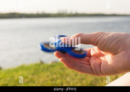 Fille avec un tri Fidget part Spinner sur sa main à l'extérieur. L'herbe verte et la rivière en arrière-plan. Banque D'Images