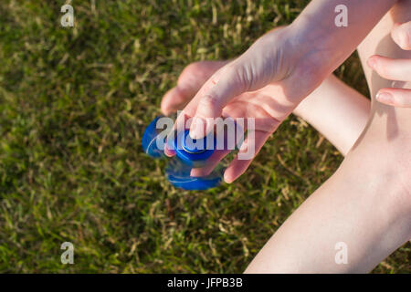 Fille avec un tri Fidget part Spinner sur sa main à l'extérieur. L'herbe verte à l'arrière-plan. Banque D'Images