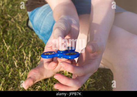 Fille avec un tri Fidget part Spinner sur sa main à l'extérieur. L'herbe verte à l'arrière-plan. Banque D'Images