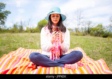 Attractive young woman dressed smartphone utilise nonchalamment assis sur une couverture colorée dans le parc. Mode de vie moderne à l'aide d'appareils mobiles portables eve Banque D'Images