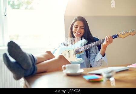 Belle fille chanter tout en jouant de sa guitare électrique avec pieds en haut du tableau Banque D'Images