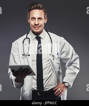 Smiling young woman une labcoat et tenant une tablette numérique seule dans un studio sur un arrière-plan gris Banque D'Images