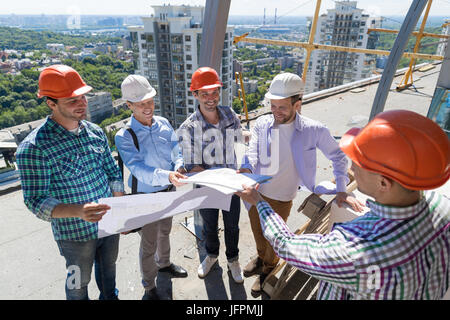 Les constructeurs sur place à la recherche sur plan PLan expliquant aux apprentis de l'entrepreneur du projet de l'équipe Banque D'Images