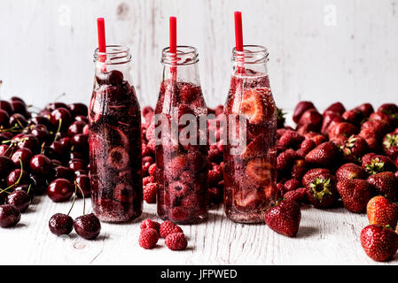 L'eau dans trois bouteilles de désintoxication aux fruits rouges sur fond de bois blanc Banque D'Images