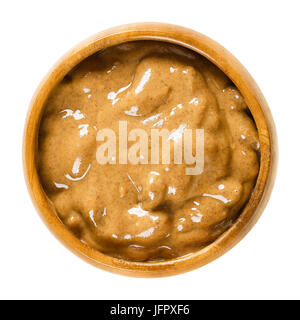 Le beurre d'amande dans un bol en bois. Brun lisse pâte faite d'aliments d'amandes. La purée de noix de Prunus dulcis. Macro photo alimentaire isolé close up. Banque D'Images