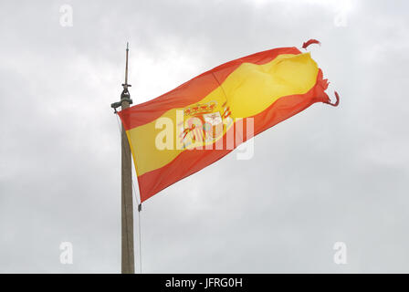 Ancien drapeau espagnol sur un poteau, ondulant dans le vent avec des nuages à l'arrière-plan, le château de Santa Barbara d'Alicante, Espagne. Banque D'Images