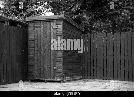 Image en noir et blanc d'un petit abri de jardin en bois sur un patio dans le coin d'un jardin sur une triste journée d'été. Banque D'Images