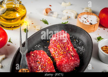 La viande, le boeuf. Lard frais dans une poêle. Les épices (sel, poivre), des légumes frais - tomates, carottes, ail, oignons. Sur une table de marbre blanc, wi Banque D'Images