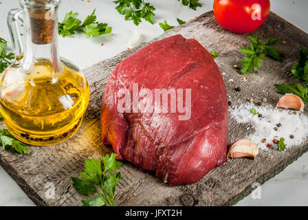 La cuisson du filet de bœuf farci. Grande pièce de filet de veau sur une vieille planche à découper, une fourchette pour la viande, les épices (sel, poivre, persil, ail, Banque D'Images