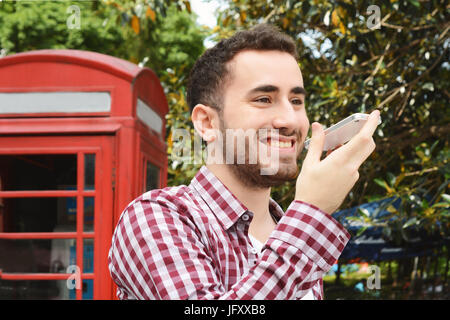 Portrait de jeune homme latin l'envoi de messages vocaux. À l'extérieur. Scène urbaine. Banque D'Images