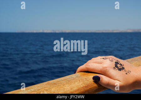 Une photographie d'une main féminine tenant la rampe d'un bateau dans la mer Méditerranée, Malte. Il y a une conception florale tatouage au henné sur le dos o Banque D'Images