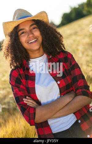 Portrait de belle et happy mixed race African American female girl child wearing straw cowboy hat et du plaid shirt et t-shirt blanc, souriant avec Banque D'Images