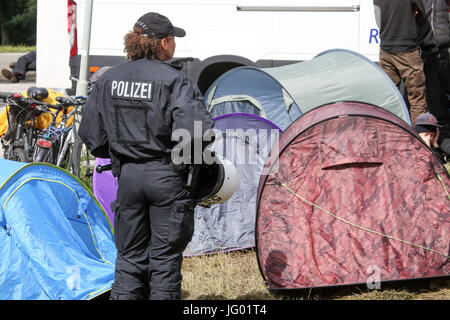 Hambourg, Allemagne. 07 juillet, 2017. Une femme agent de police se tient derrière certaines tentes à l'entrée de l'Entenwerder Elbpark en face de la gare Ferry Entenwerder dans le quartier de Rothenburgsort, Allemagne, 02 juillet 2017. Selon les déclarations de militants, la police de Hambourg a bloqué la construction d'un camp de protestation contre le sommet du G20, qui avait été approuvé par un tribunal administratif. Photo : Bodo Marks/dpa/Alamy Live News Banque D'Images