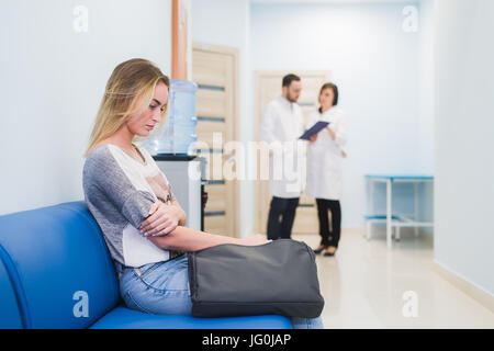 Jeune femme assise à nerveux remplissage couloir de l'hôpital en attente pendant que deux médecins qui parlent sur un backgroud Banque D'Images