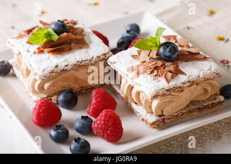 Millefeuille au chocolat avec la crème à café, les framboises et les bleuets sur une plaque horizontale. Banque D'Images