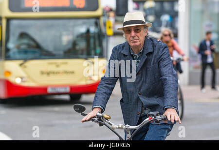 Âge moyen à la suave élégant pour homme plus âgé dans un chapeau d'été tenue en jean et le vélo sur une route très fréquentée. Banque D'Images