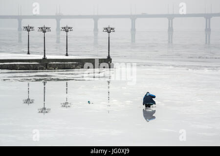 Le pêcheur est la pêche sur la glace d'une rivière gelée dans un matin brumeux. De Dnepropetrovsk, Ukraine Banque D'Images