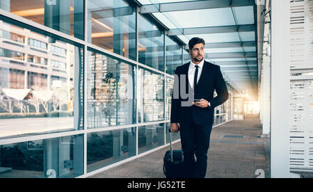 Beau jeune homme marchant à l'extérieur de la station de transport public. Caucasian business traveler avec valise à l'aéroport. Banque D'Images