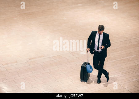 Vue de dessus shot of young businessman standing à l'aéroport avec valise et à l'aide de téléphone mobile. Les voyageurs d'affaires reading text message cell phone Banque D'Images