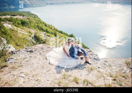 Superbe jeune couple assis sur le bord de la falaise avec un beau paysage sur l'arrière-plan. Banque D'Images