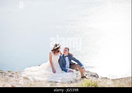 Superbe jeune couple assis sur le bord de la falaise avec un beau paysage sur l'arrière-plan. Banque D'Images