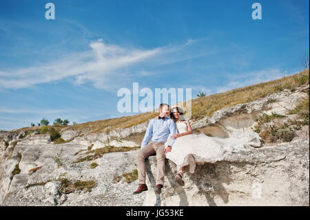 Superbe jeune couple assis sur le bord de la falaise avec un beau paysage sur l'arrière-plan. Banque D'Images