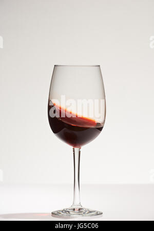 Vin rouge d'agitation sur le verre. Vin rouge en agitant son socle en verre isolé sur fond blanc Banque D'Images