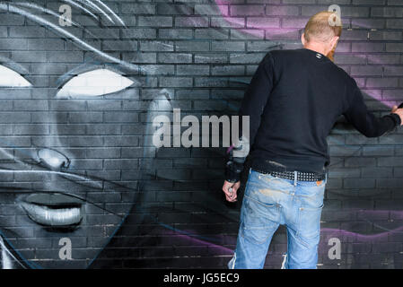 Une femme peinture artiste graffiti sur un mur avec les cheveux au vent. Banque D'Images