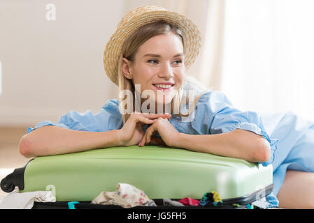 Smiling young blonde woman in hat valise d'emballage et à l'écart, l'emballage assurance concept Banque D'Images