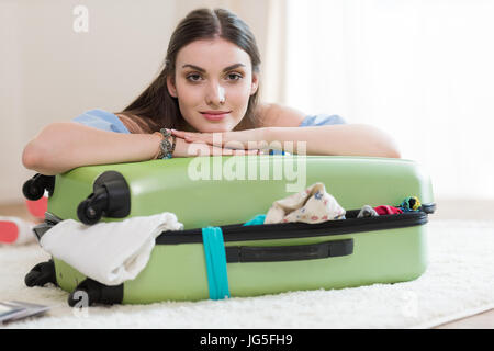 Belle jeune brunette woman packing suitcase et looking at camera, emballage assurance concept Banque D'Images
