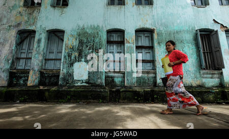 Une femme en costume traditionnel coloré marche dernières sur un vieux bâtiment de couleur verte au centre-ville de Yangon, Myanmar Banque D'Images